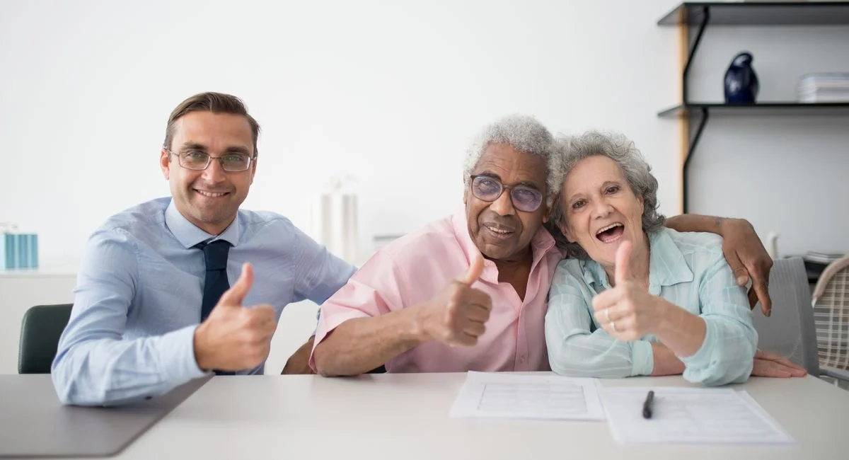 Elderly couple with consultant giving thumbs up in an office setting, showcasing positive interaction.
