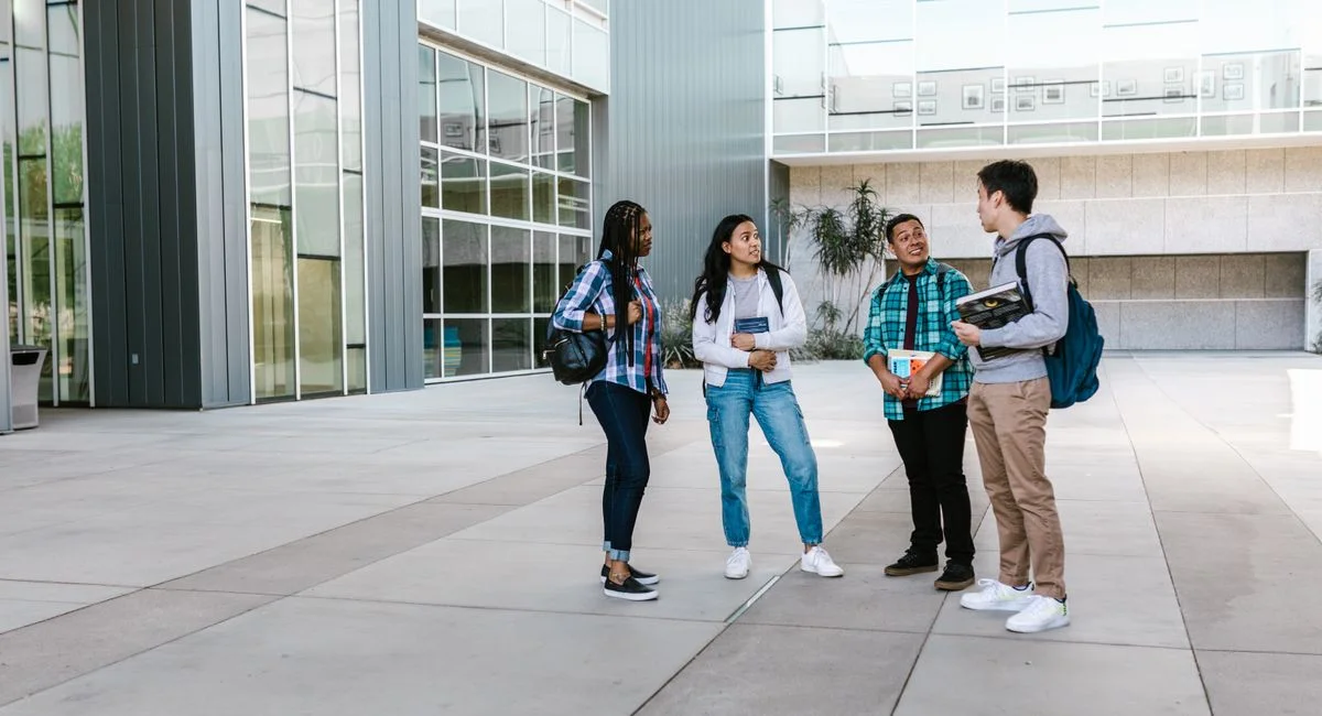 A diverse group of college students chatting outside a modern university building.