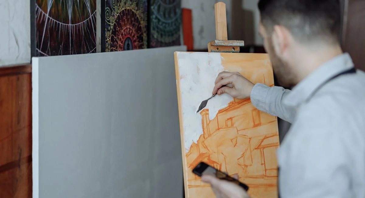 Artist working on canvas in studio, creating abstract art with paint and brushes.