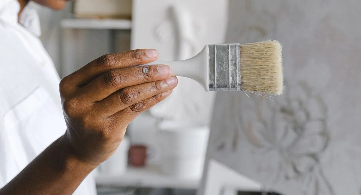 Detailed view of an artist's hand holding a paintbrush in a studio setting, focusing on creative work.
