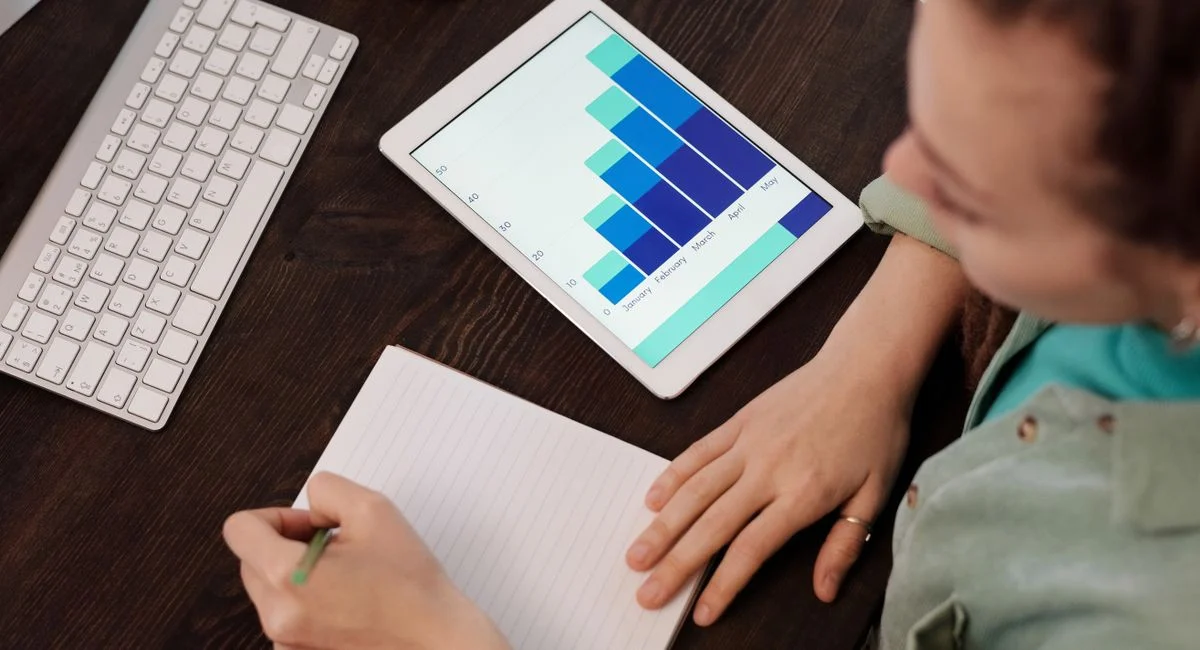 A woman taking notes while analyzing data on a tablet, ideal for business and technology themes.