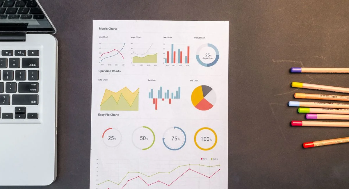 Top view of charts and colored pencils on a desk next to a laptop, perfect for business or education themes.